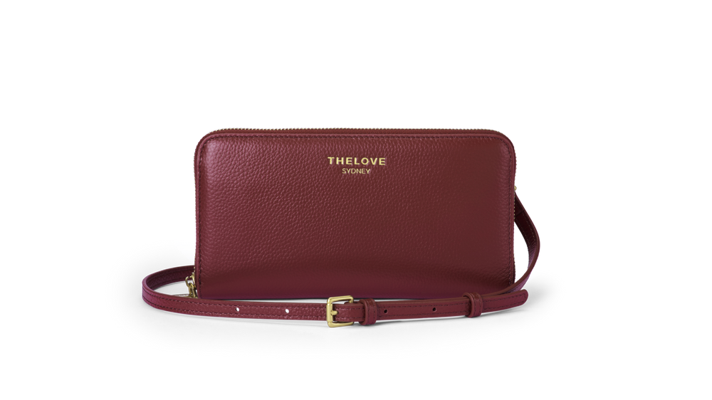 Maroon leather clutch bag with gold strap on a white background